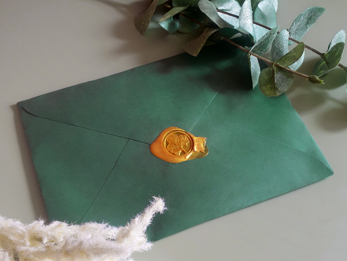 a green envelope with a golden wax seal with a ginkgo engraved in it