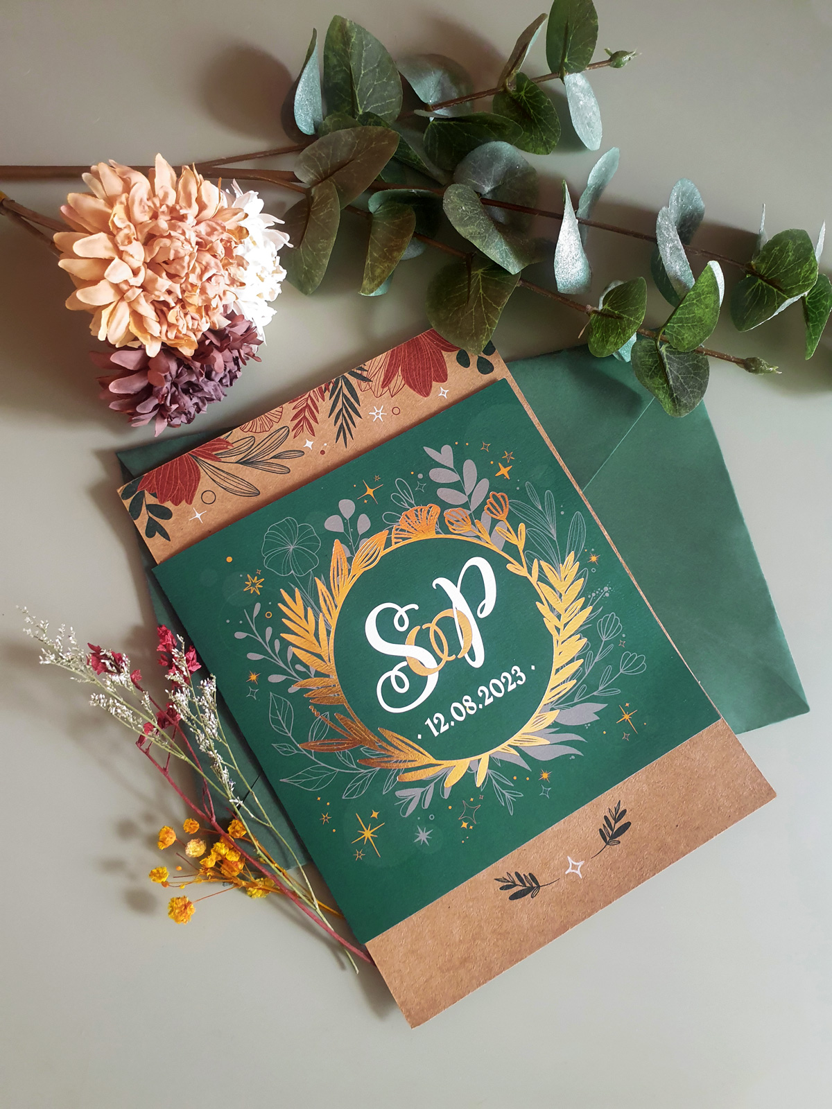 Wedding Invitation with golden and green details in front of a color matching envelope